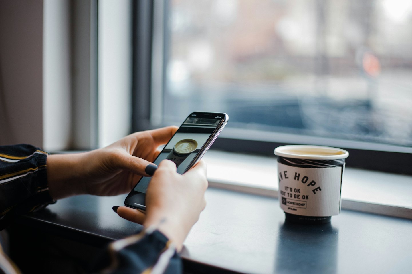 Hands holding smartphone displaying coffee art next to real cup.