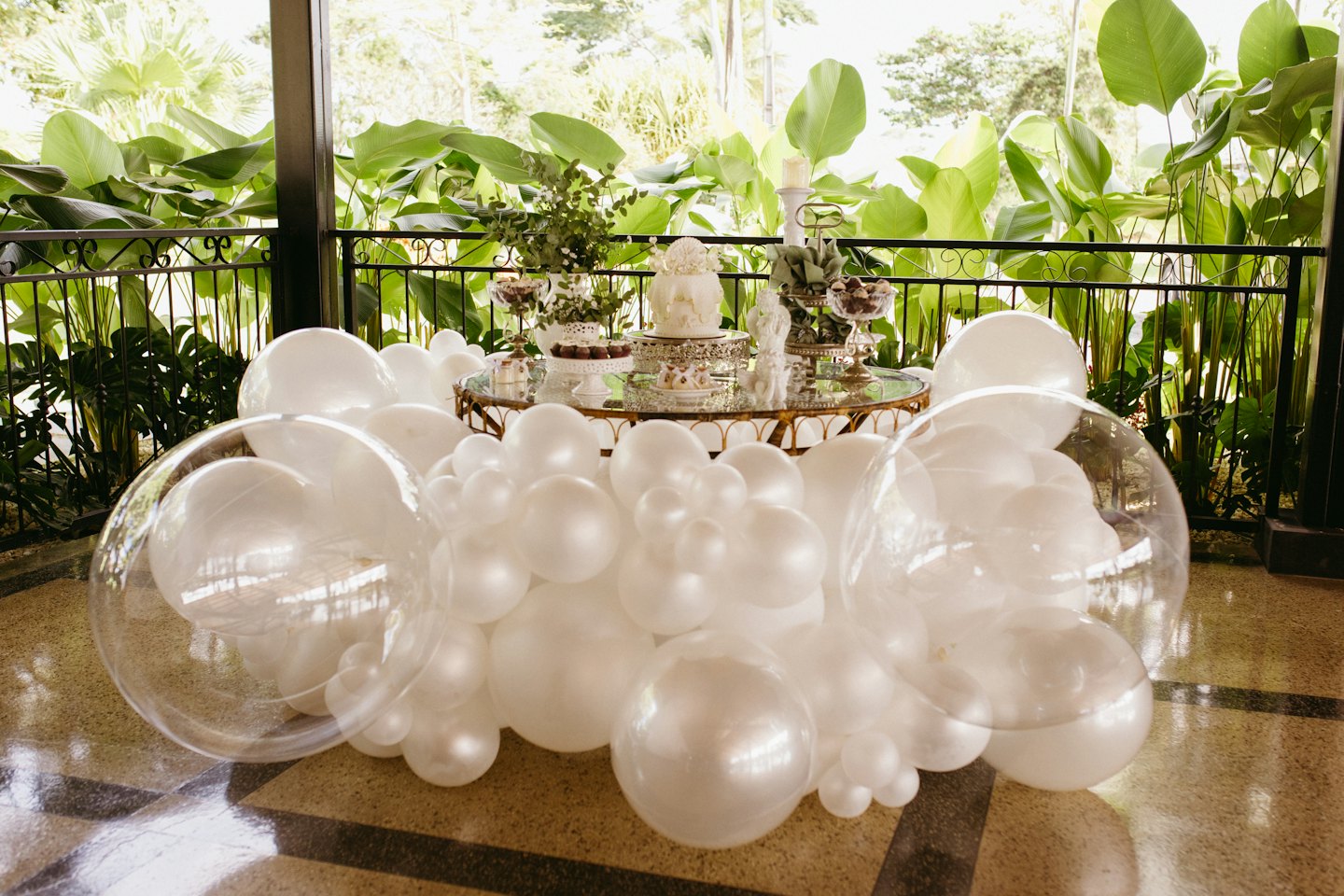 White balloon garland frames a dessert table with a tiered cake.