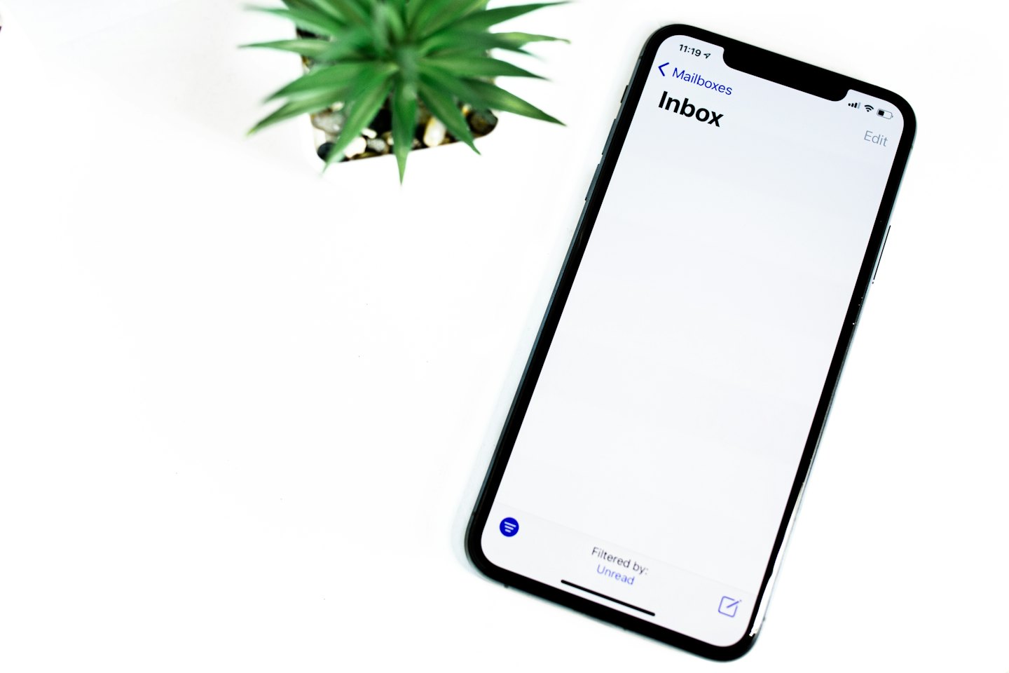 Black smartphone displaying an email inbox on a white surface.