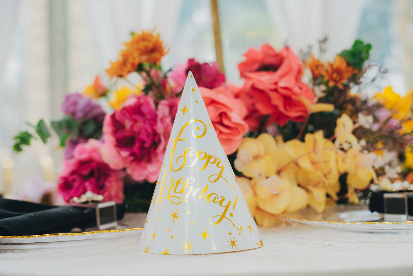 Birthday hat with gold text sitting on a tablecloth.